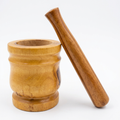 A wooden mortar and pestle set on a clean white background. The mortar is made of light tan wood with a flared rim and a small carved detail on the side, while the pestle is a medium brown wood with a visible grain pattern.